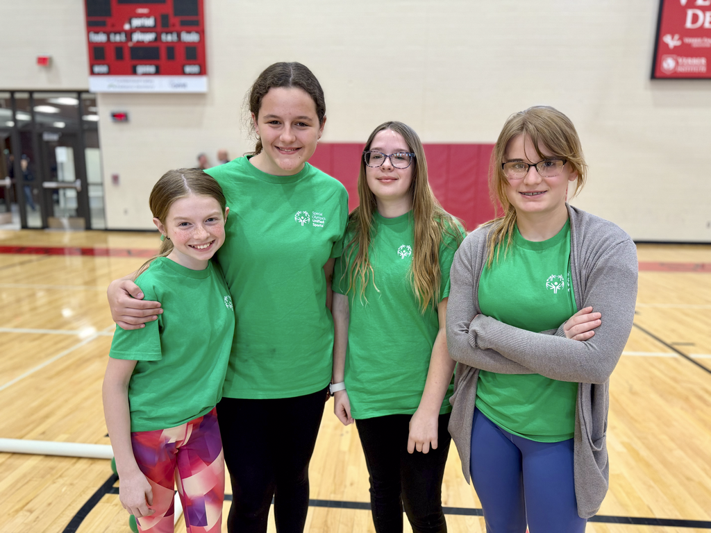 Four middle school students in green Unified Sports shirts pose together in a gym during a unified bocce game.
