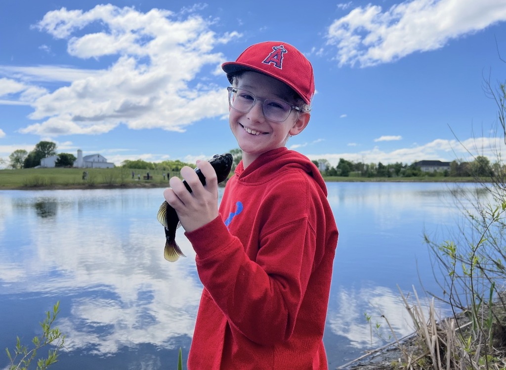Student holding a small fish by a pond during Middlesex Elementary’s 5th grade Environmental Ed Day.