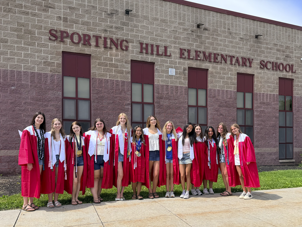 Students wearing graduation gowns gather outside of Sporting Hill Elementary School during a Senior Walk.