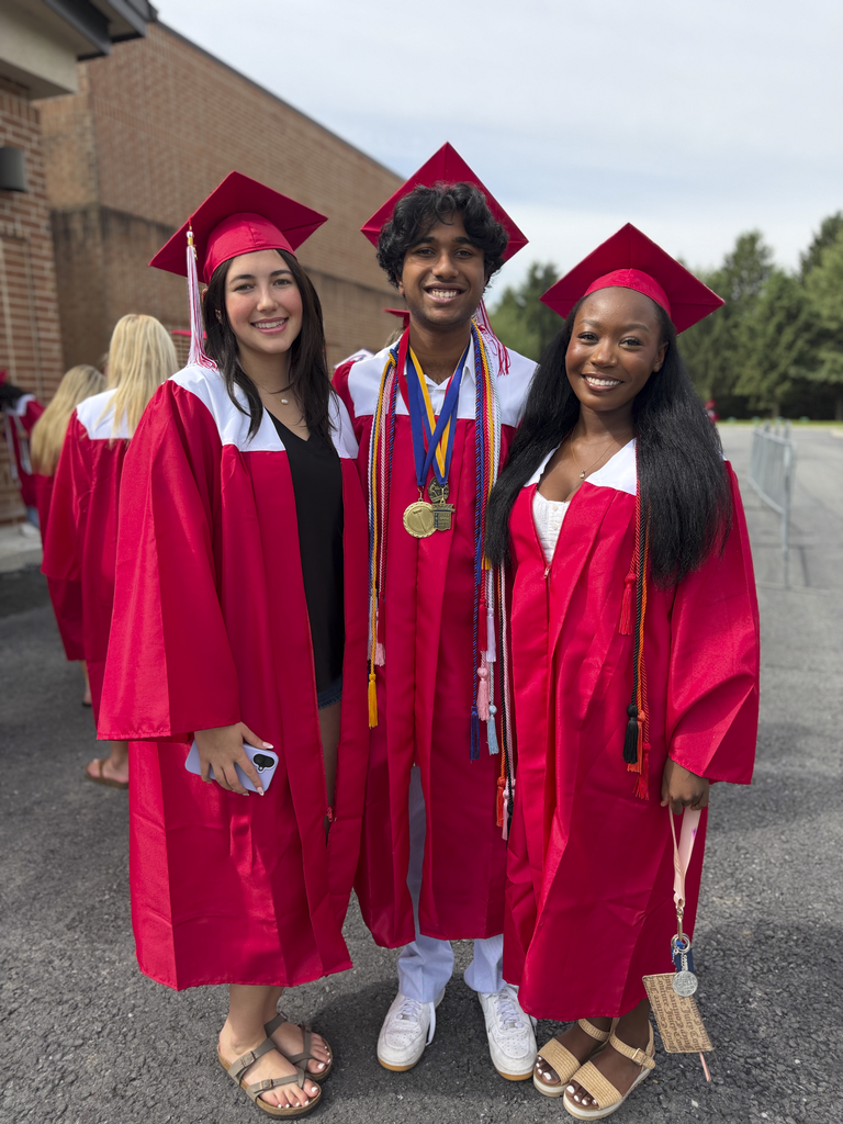 Three students standing outside with their graduation caps and gowns.
