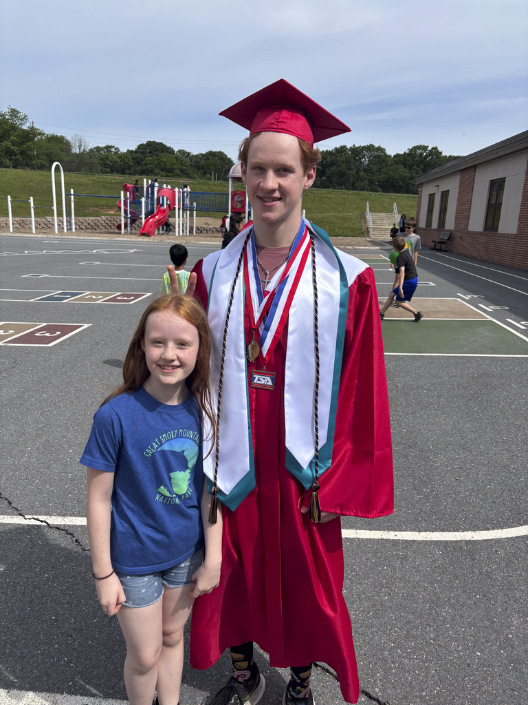 A student wearing a graduation cap and gown poses with their younger sibling outside on the playground.