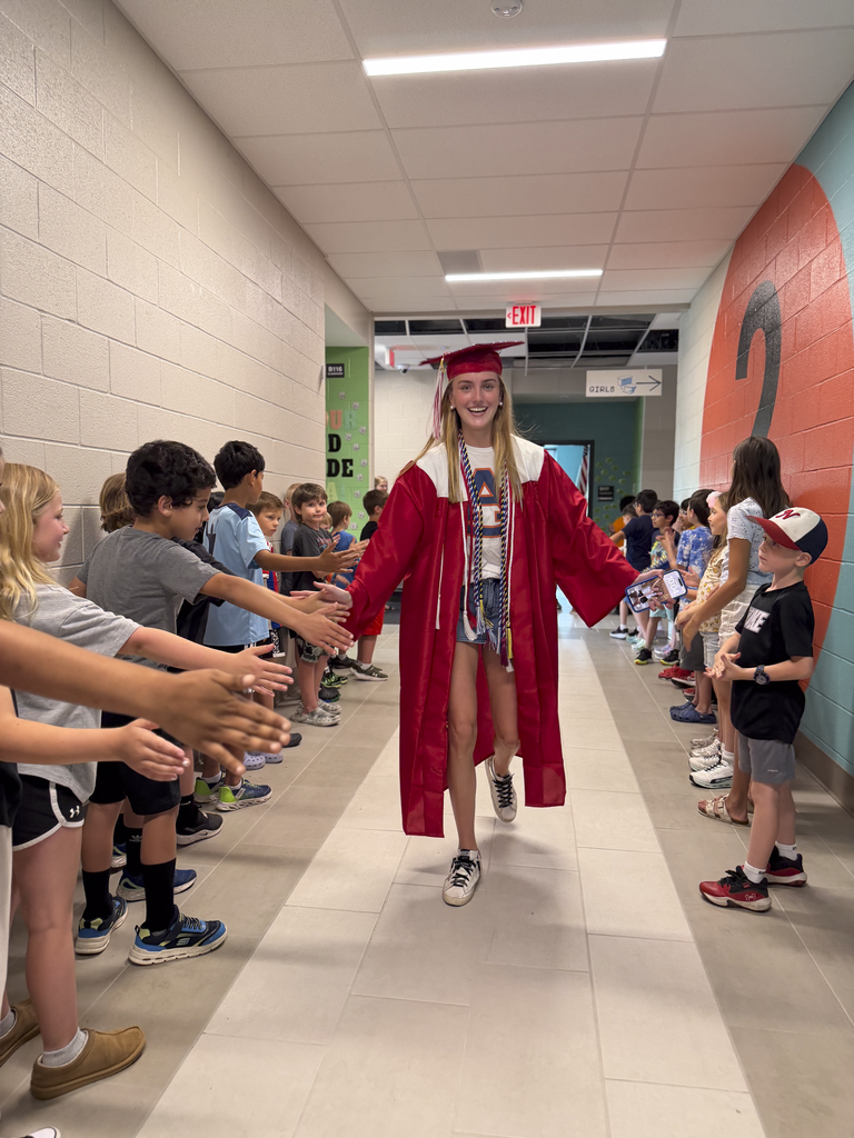 A student walks through a hallway in her graduation cap and gown, giving high-fives to younger students.