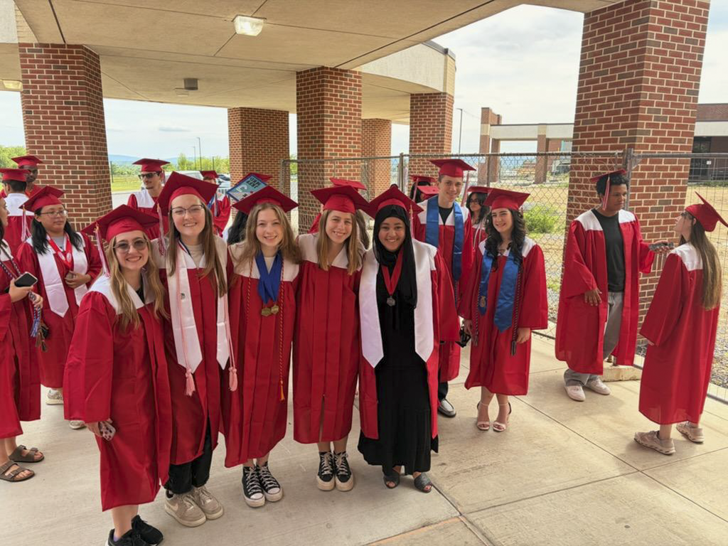 Students wearing graduation caps and gowns poses for a group picture outside Eagle View Middle School during a Senior Walk.