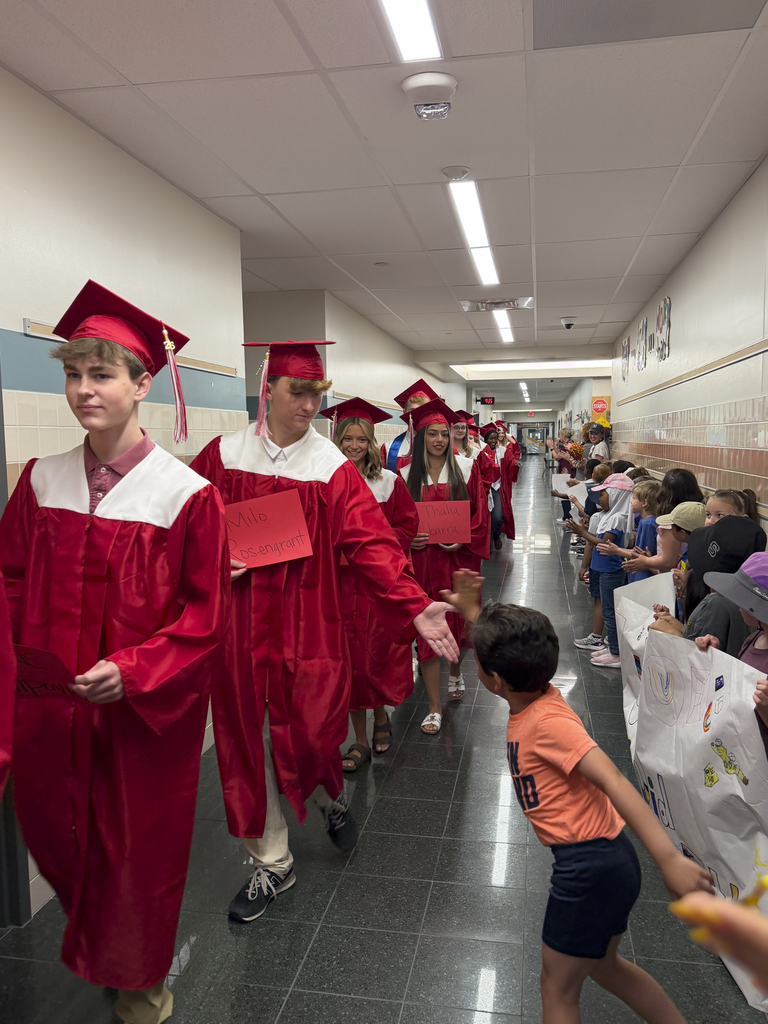 Students walk the halls of their old elementary school in their graduation caps and gowns during a Senior Walk and giving high-fives.