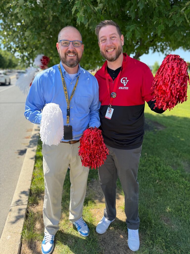 Two District Administrators pose for a picture holding pom poms as they celebrate the last day of school for students.