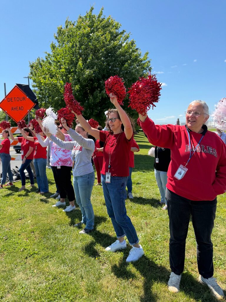 District Office staff hold pom poms and cheer as student's leave campus on their last day of school.