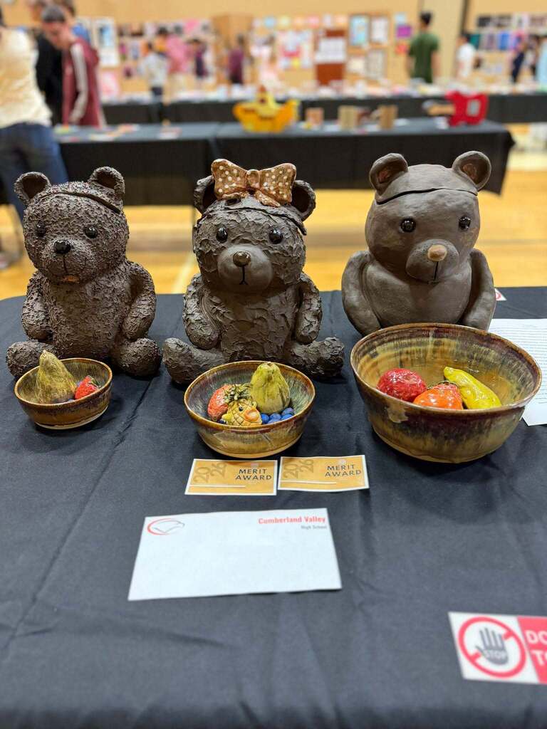 Three ceramic bear sculptures on display with bowls of fruit, awarded merit prizes at a national level.