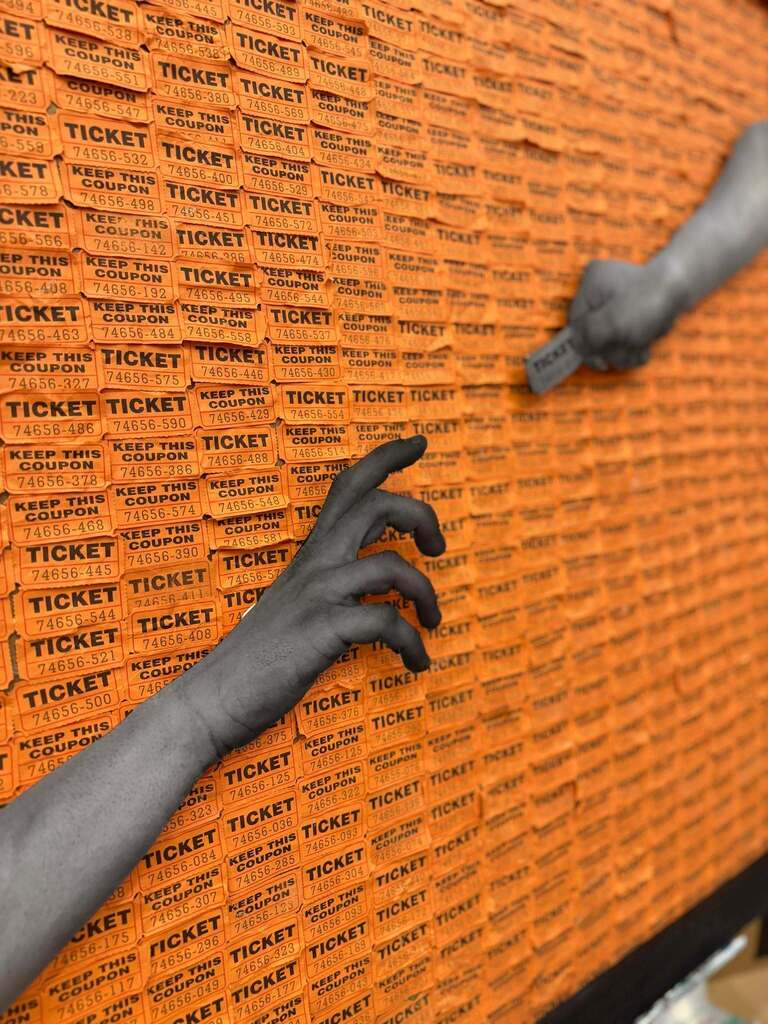 Wall covered in orange raffle tickets, with two hands reaching to pull tickets from the display.