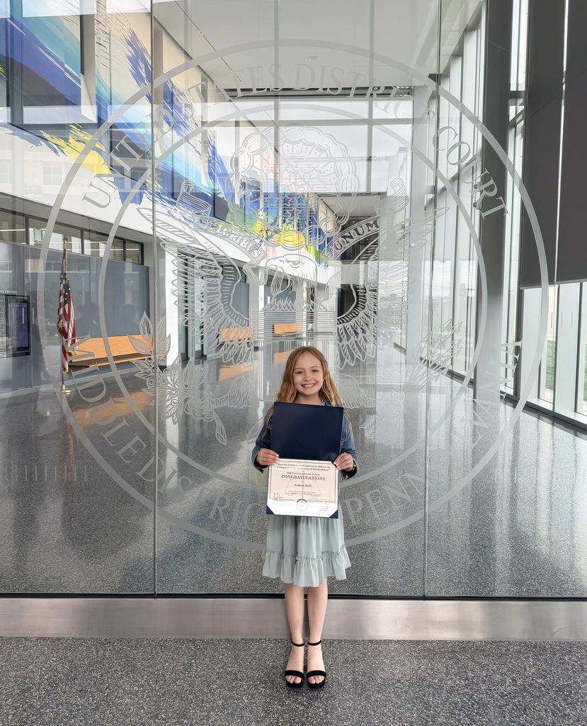 Eagle View Middle School student, Aubree Kohl, holds a certificate and award folder while standing in front of the United States District Court seal inside a courthouse lobby after earning a Top 10 finish in a federal essay contest.