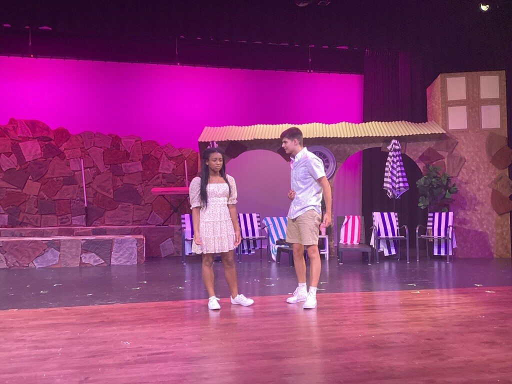 Two students rehearse a scene from High School Musical 2 JR onstage in front of a resort-themed set.