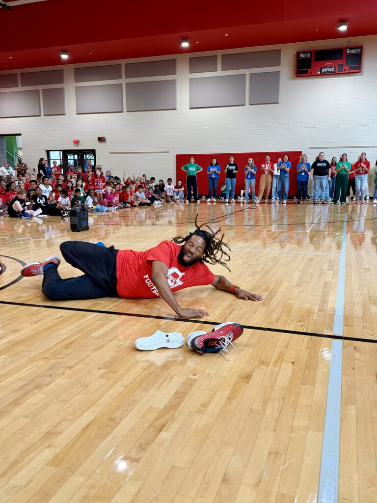 A staff member participates in a game during Winding Creek Elementary’s House Assembly while students and staff watch from the gym sidelines.