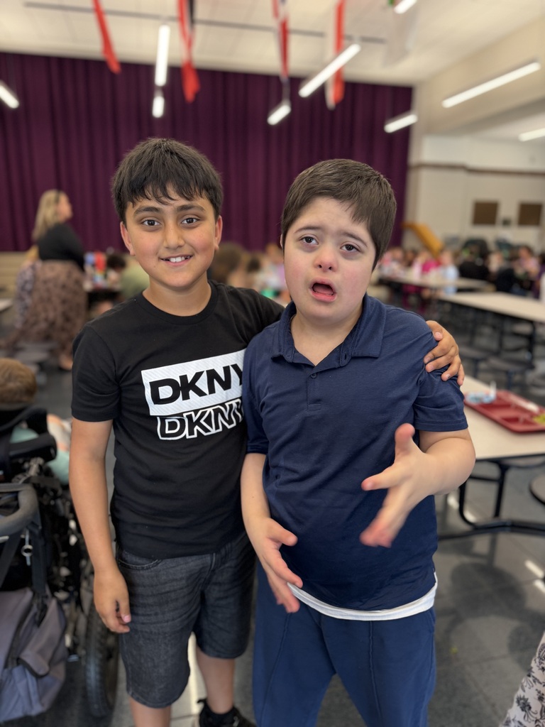 Two students smiling and standing together in a school cafeteria during lunch