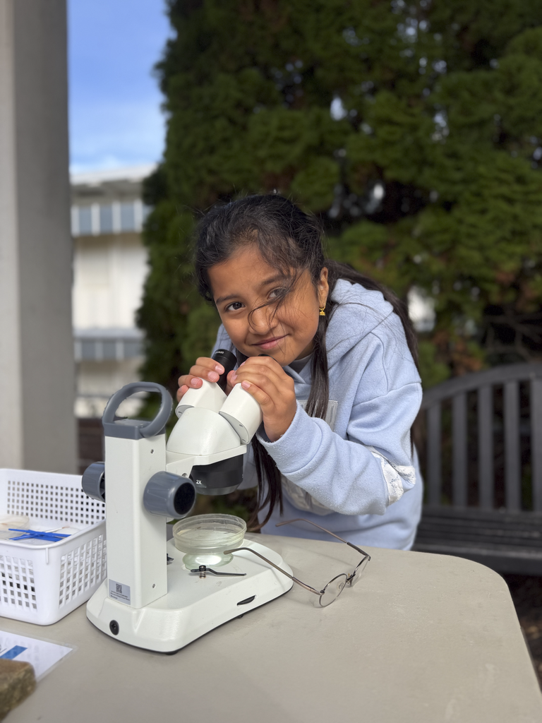 CV fifth-grade poses for a smile while holding on to a microscope that has as petri dish on it.