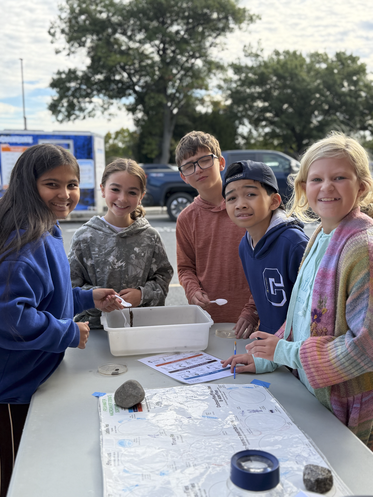 CV Fifth-grade students work outdoors to examine and identify freshwater organisms using trays, tools, and identification guides during a Stroud Water Research activity.