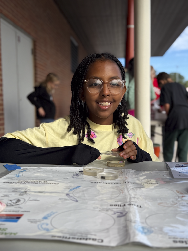 A CV fifth-grade student holds a magnifying glass over a petri dish to inspect fresh water insects.