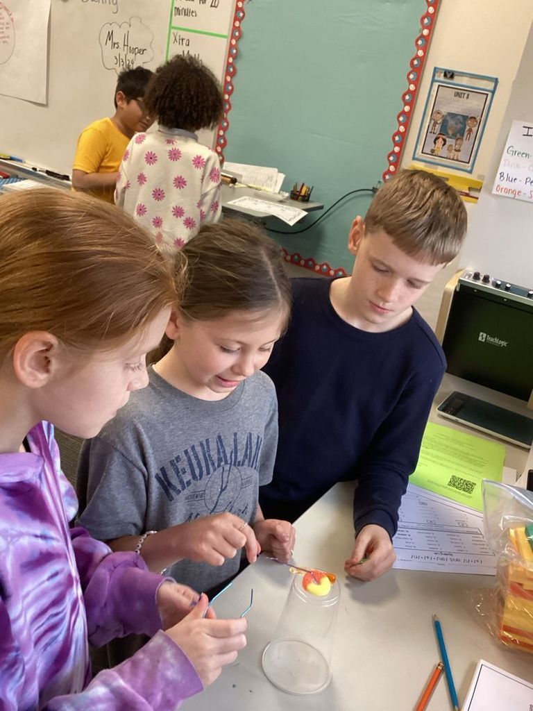 Three students using paper clips to rescue a gummy worm as part of a science project.