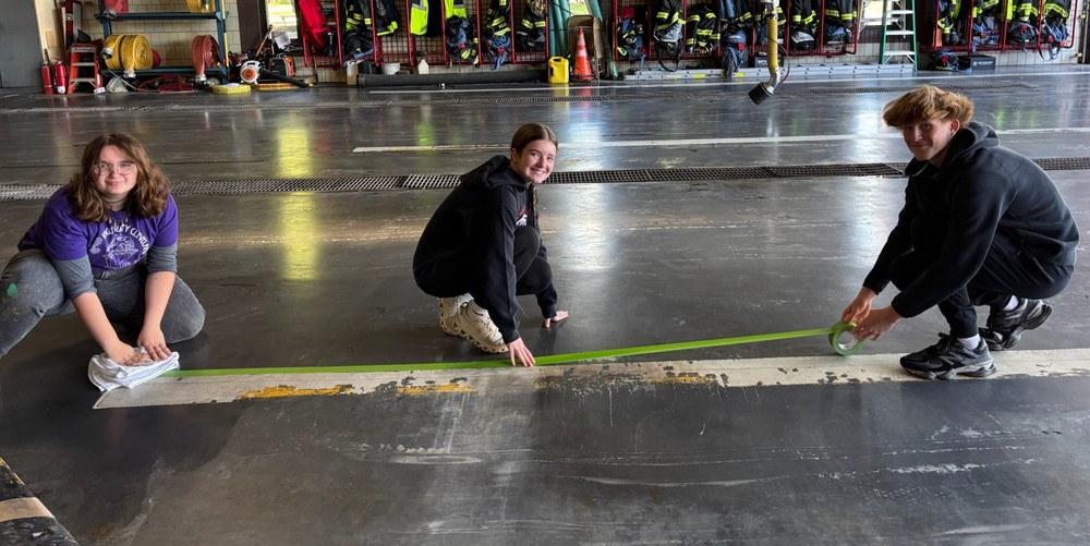 Students set down tape in preparation to paint stripes on fire station garage floor.