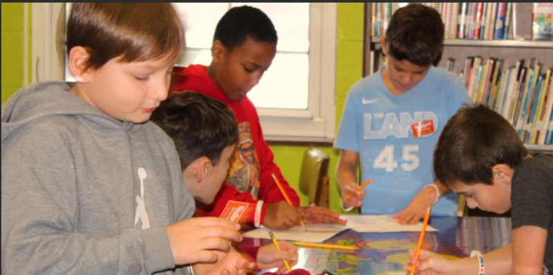 Boys working on a project around a table. 