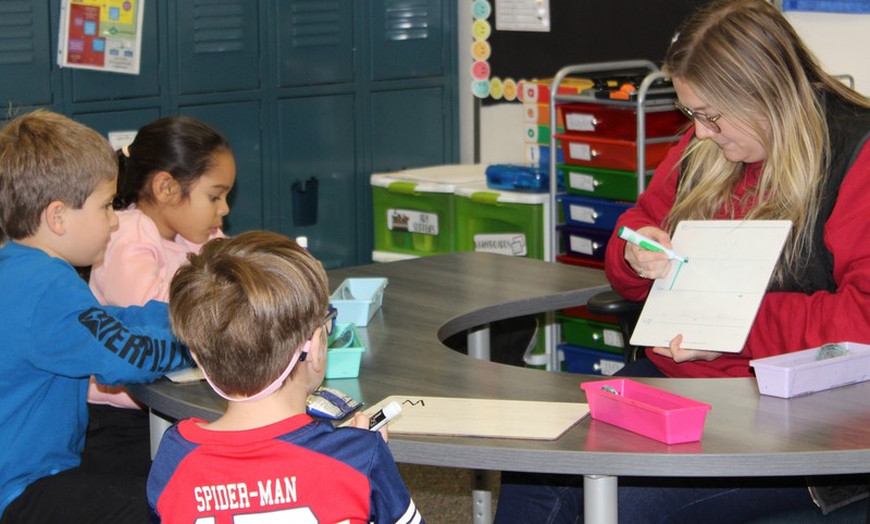 Three students working with teacher at a table. 