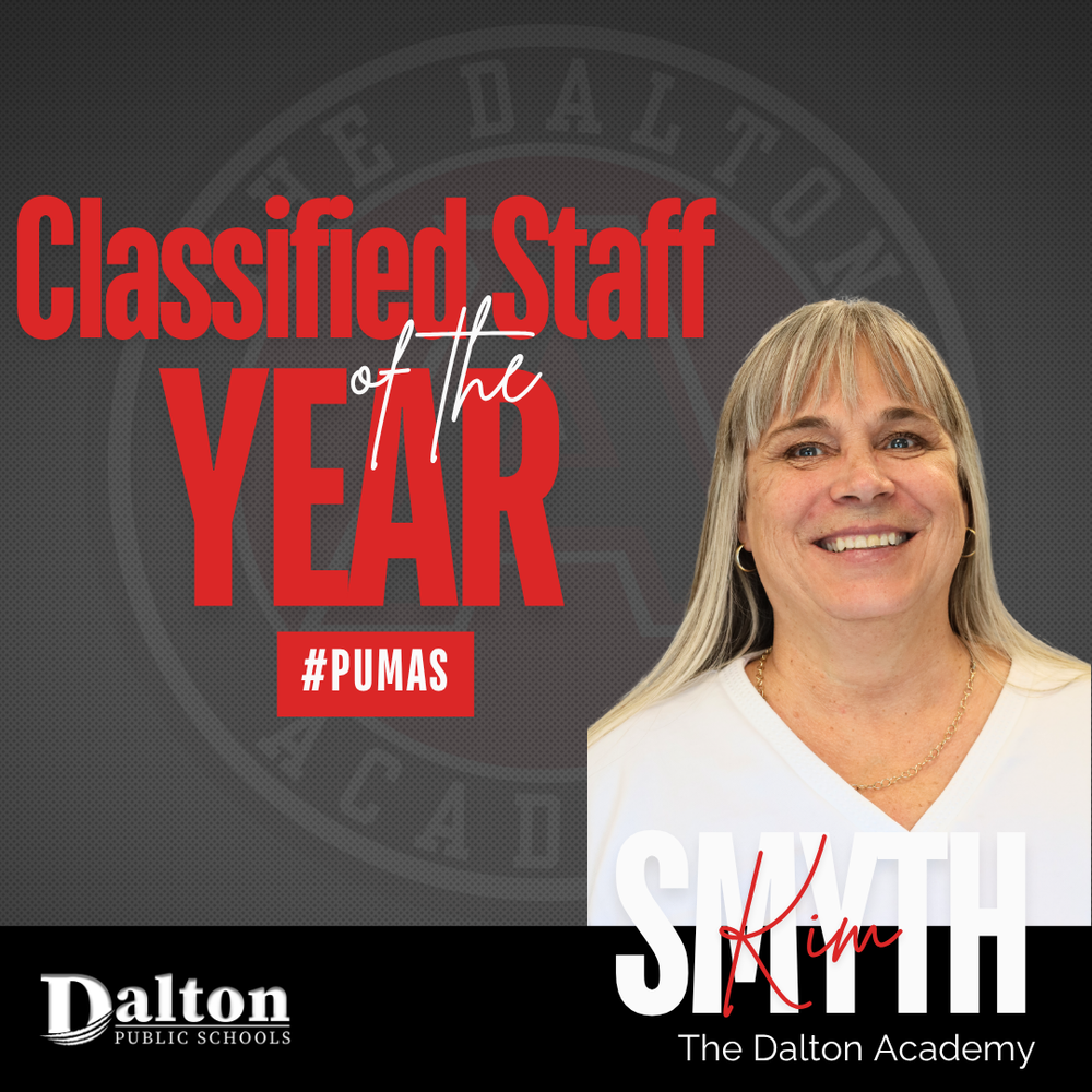 A square promotional award graphic set against a dark gray background with a faint seal of The Dalton Academy watermarked in the center. A portrait of smiling staff member Kim Smyth appears on the right side. On the left, bold red text reads "Classified Staff of the Year" above a red box displaying the hashtag "#PUMAS". Along the bottom, the surname "SMYTH" is written in bold white lettering with "Kim" overlaid in red script, flanked by the Dalton Public Schools logo and "The Dalton Academy."