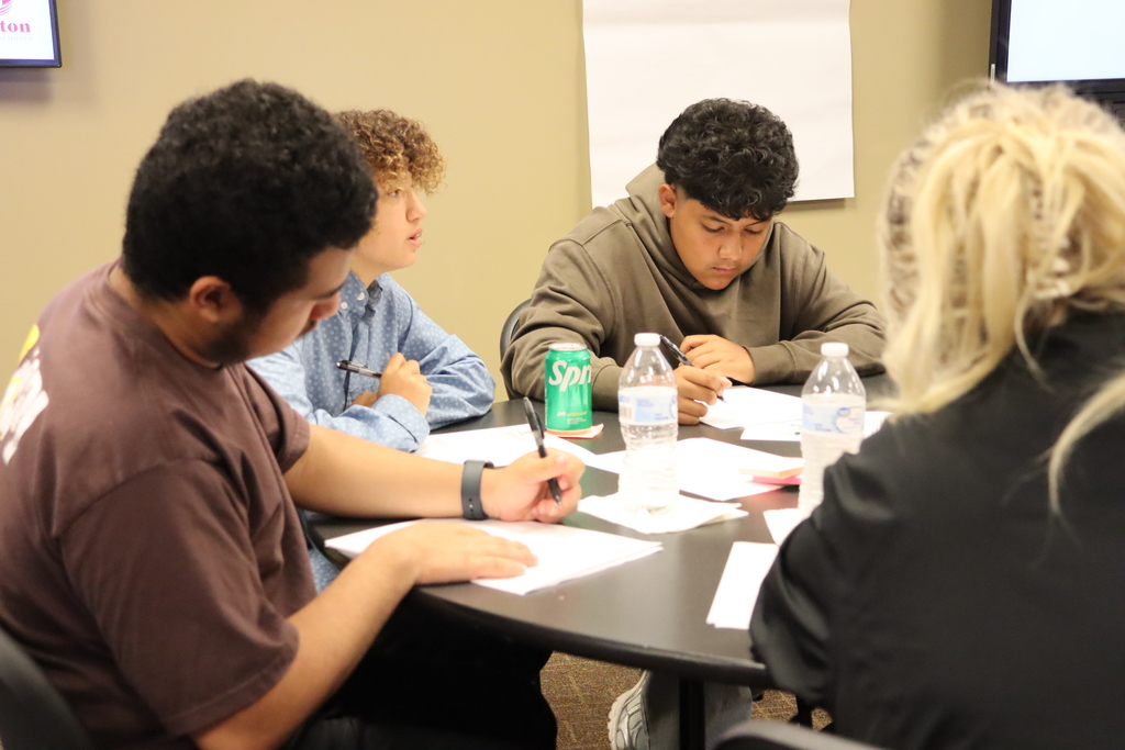 Four students work together at a table, writing notes and discussing ideas during the Student Advisory Council meeting.