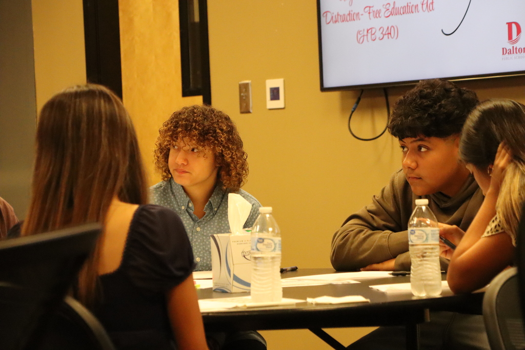 A group of students sit together at a table, listening intently during a discussion at the Student Advisory Council meeting.
