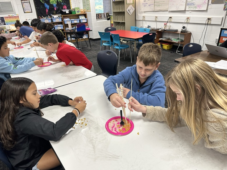 Students trying to pick up food using chopsticks