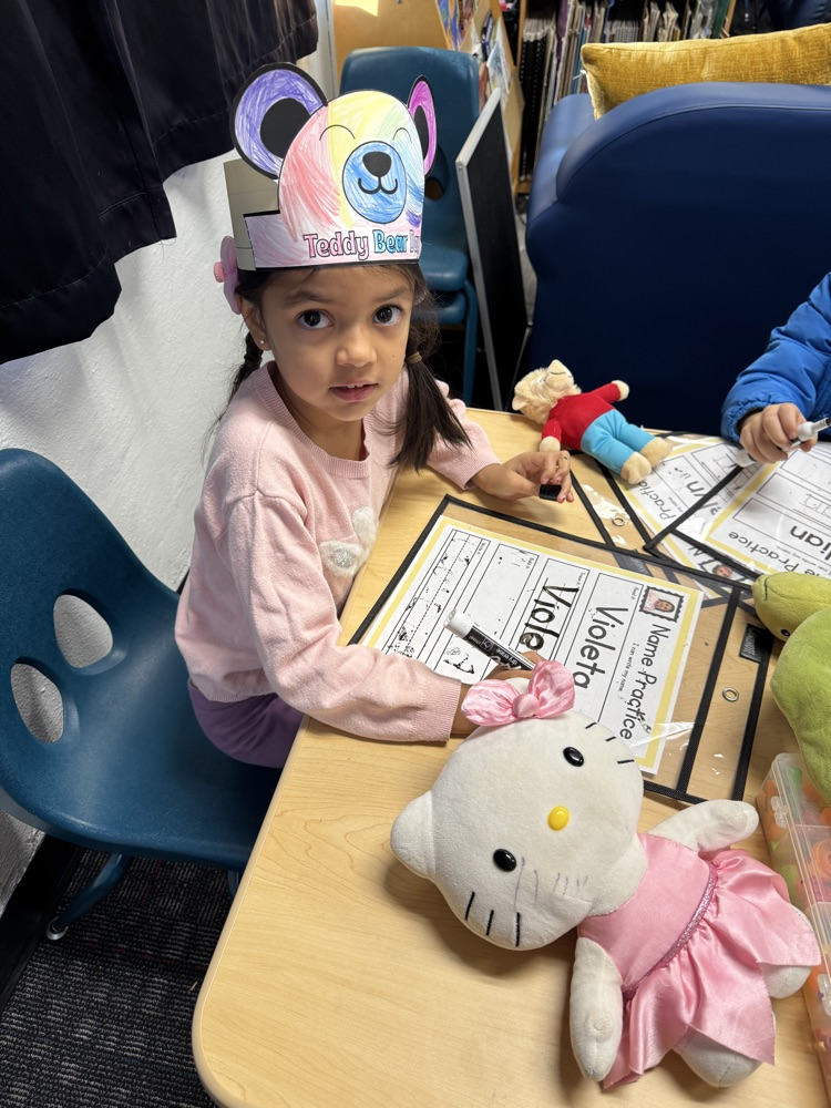 A student practicing writer name with her stuff animal