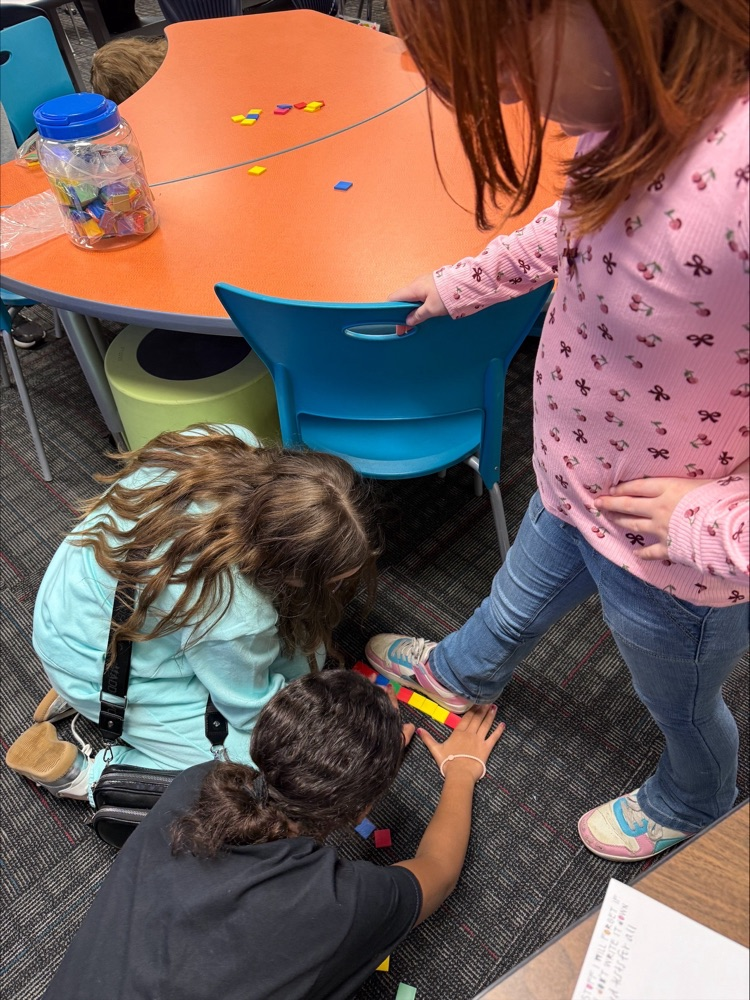 Two students measuring another student’s shoes with cubes  
