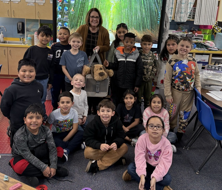 Image shows a group of students and a teacher holding a stuffed dog  
