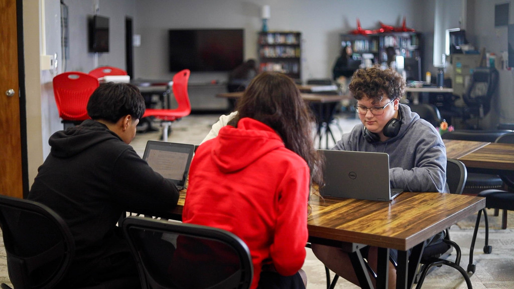 Cyber Academy students sit together at a table, focused on their laptops while working collaboratively in a classroom setting.