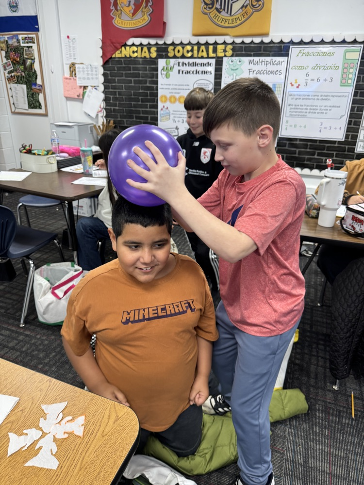 A student rubs a balloon on a classmate’s head to observe electron transfer 