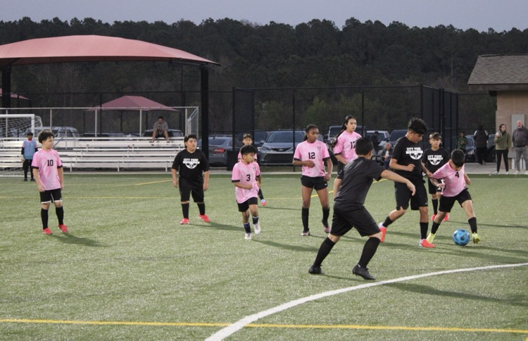 A soccer player kicking the ball in between defenders 