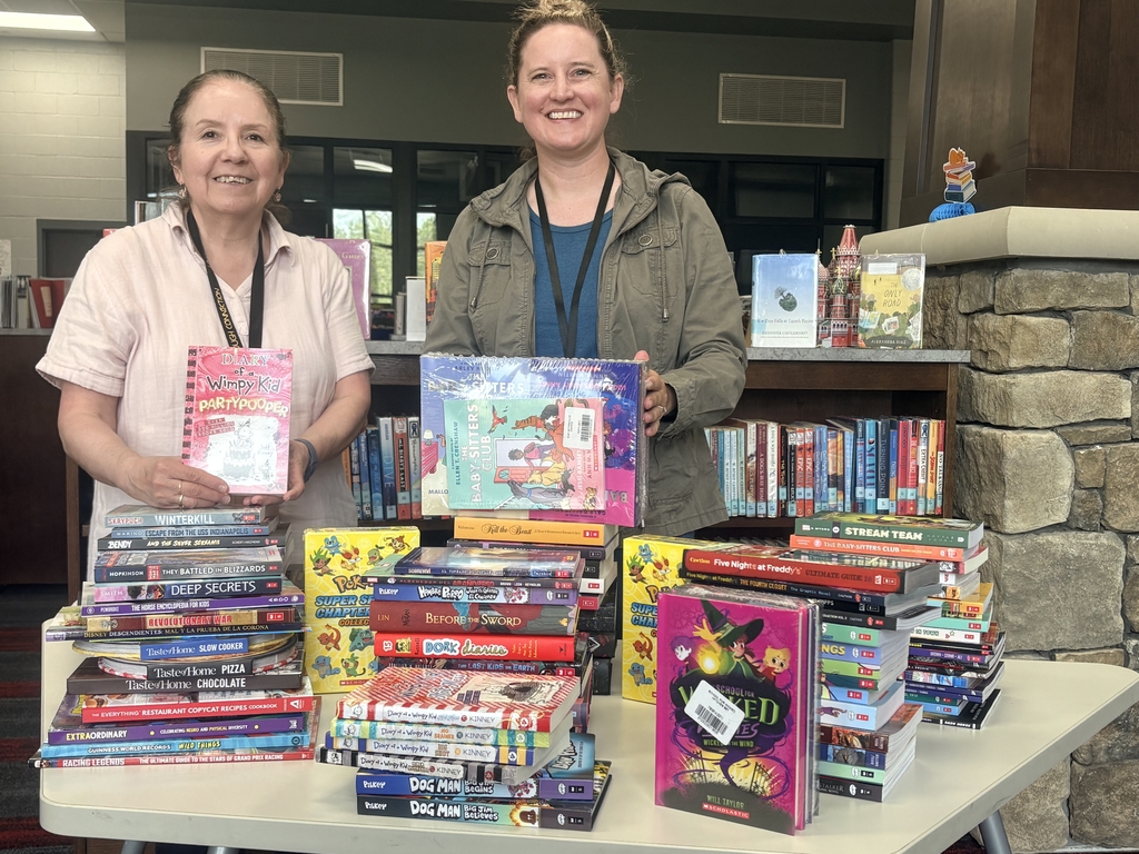 Keri Faw and Ivelisse Gonzalez posing with stacks of books from the book fair