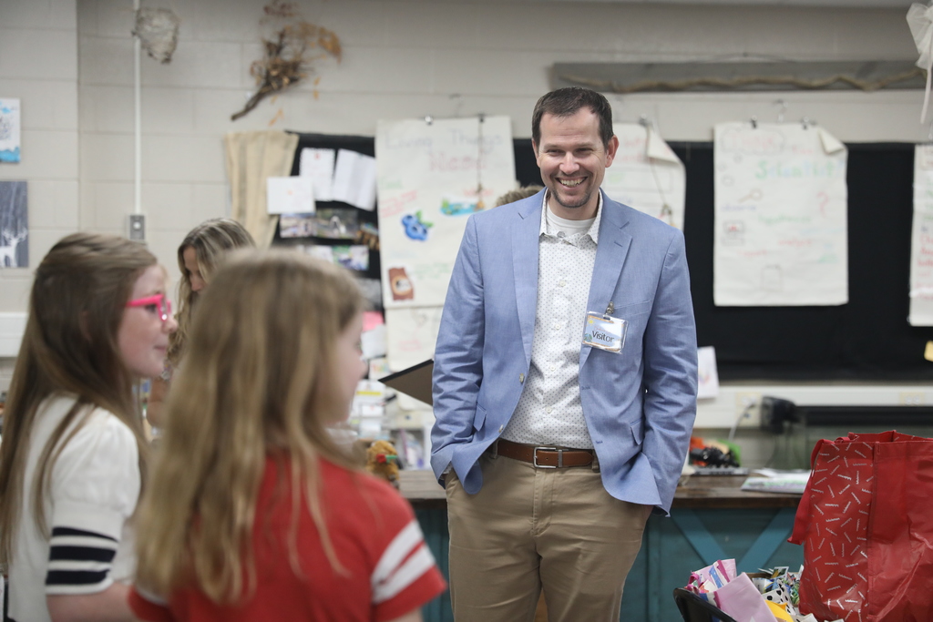 A male teacher smiles at students who are presenting.