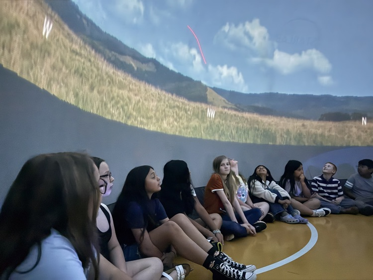 Studebts inside thr Star Lab looking up at a projected sky and landscape scene