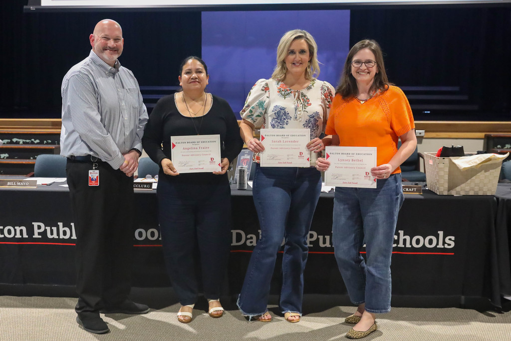 Four adults stand together at a Dalton Public Schools boardroom, smiling and holding certificates of recognition. Three women display their awards while a man stands beside them, with Dalton Public Schools signage and a meeting table visible in the background.