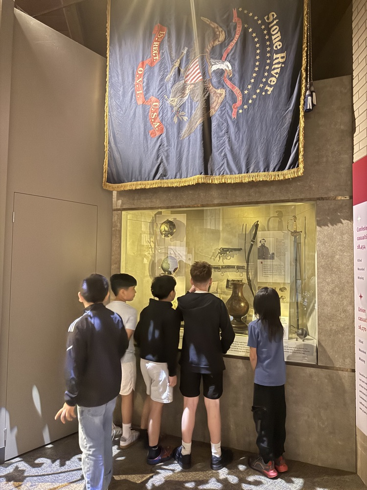 Students stand at a museum display case viewing Civil War artifacts beneath a large “Stone River” banner.