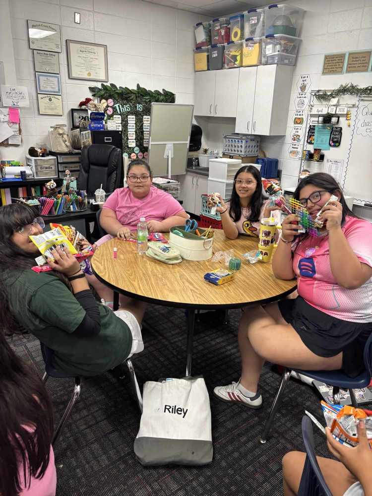 Four girls in the classroom sitting on their desks holding their prizes 