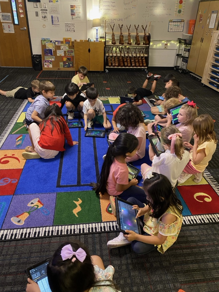 A group of students sitting on the ground with their iPads working on their music 