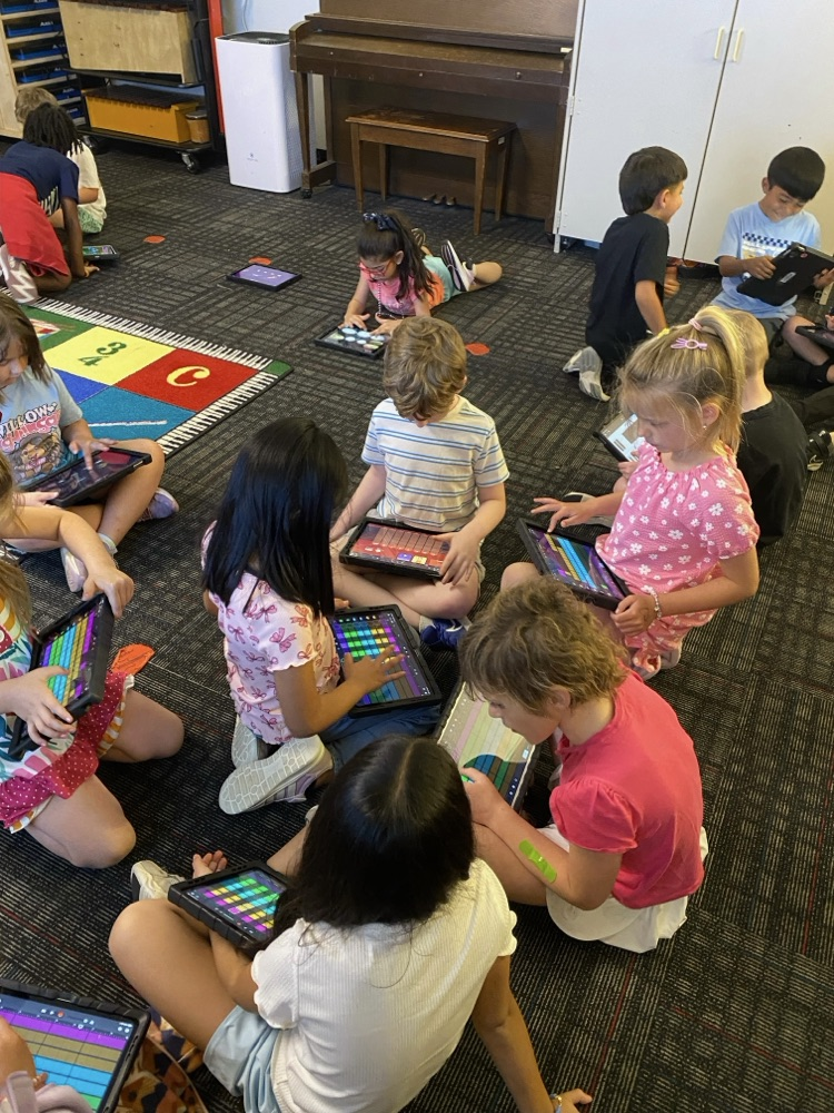 A group of students sitting on the ground working on their music with their iPads  