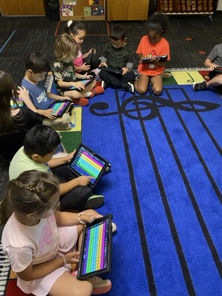 Students during around the music rug working on their music with their iPads 