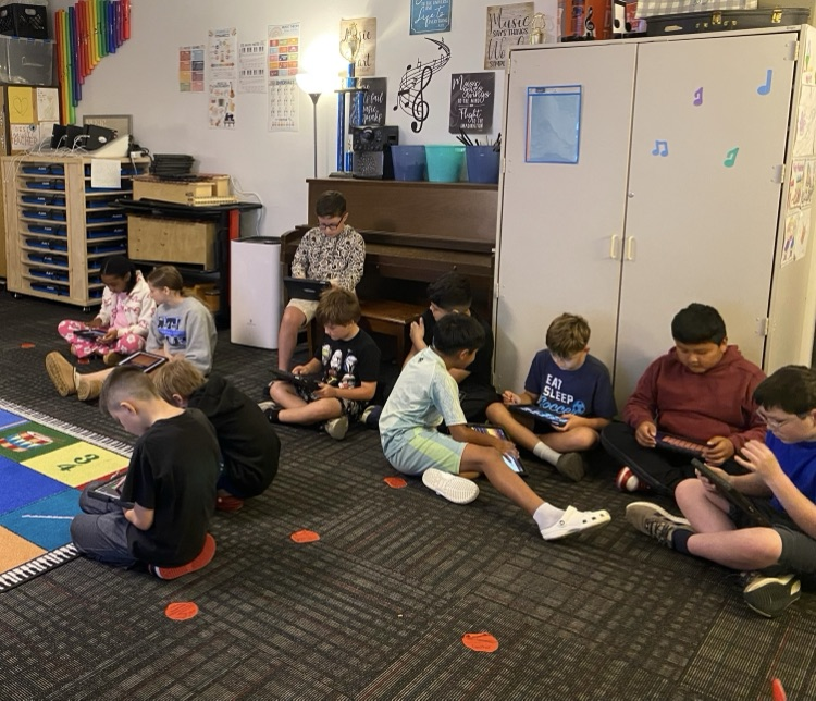 Fourth graders sitting on the ground composing their music on their iPads 