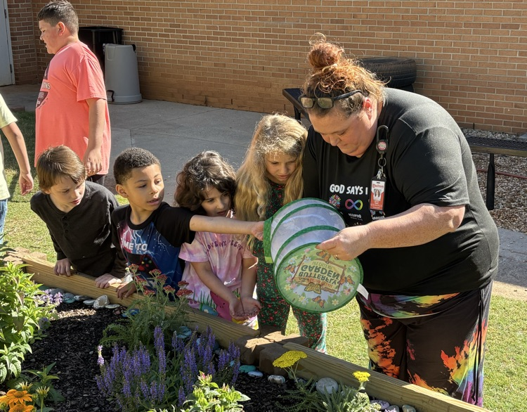 A teacher holding the butterfly net to release the butterflies in the garden with four students standing next to her watching 