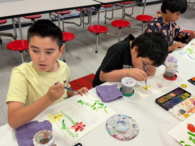 Two students sitting in the cafeteria painting flowers 