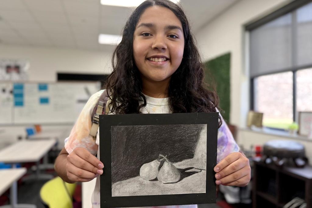 Student journalist Sofia Hernandez-Lopez stands smiling while holding a piece of artwork connected to her published GPB story and podcast. The image celebrates her achievement as an HCMS student featured by Georgia Public Broadcasting for her independent journalism work.
