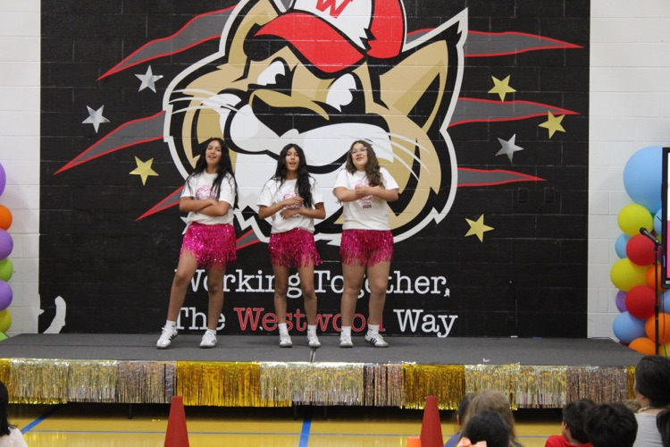 Three students dressing in pink dancing on stage 