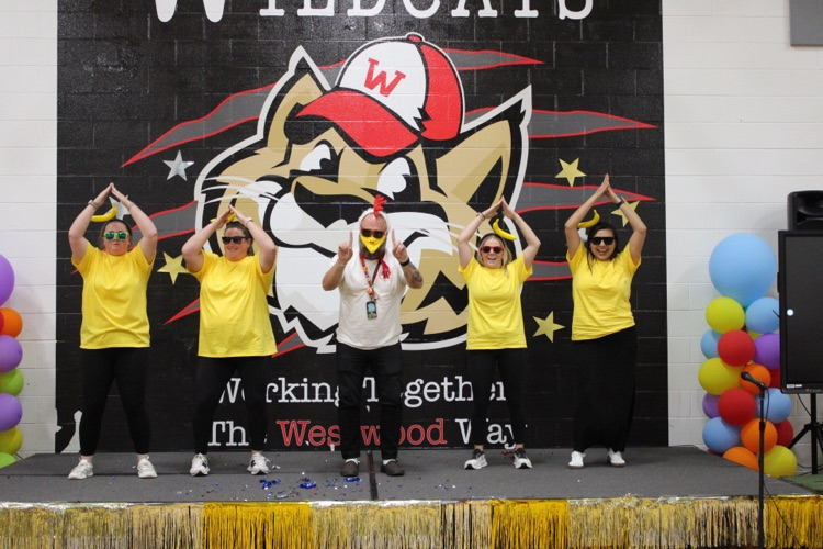 Five teachers dressing up like chickens dancing on stage 