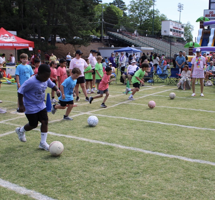 A group of students racing each other while kicking a soccer ball 