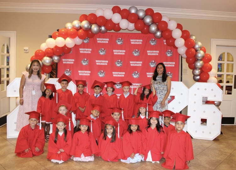 Mrs. Hinojosa’s and Ms. Lemus’ class wearing their caps and gowns for graduation standing in front of the ballon arch and backdrop decorations 